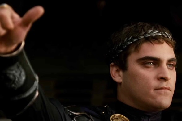 Screenshot from the 2001 movie gladiator. Here Joaquin Phoenix is playing the evil emperor Commodus. He is looking off to the right and about to make a thumbs up or thumbs down indication.