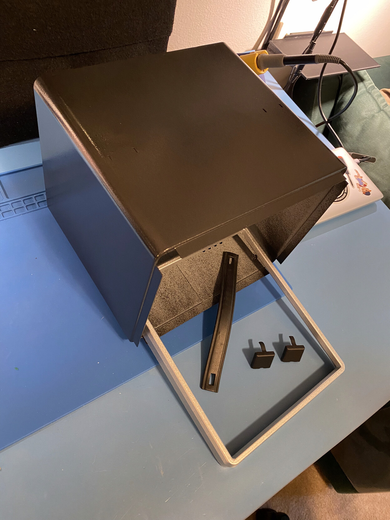 Three-quarters view of a signal generator box-style case restored and painted hammered black, along with restored flat-black enamel carrying strap attachments, and restored silver front panel frame. The case is pressed steel, the frame is cast aluminium. The inside of the case has been left primer grey.