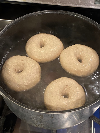 four bagels boiling in a big pot on a stovetop. four bagels boiling in a big pot on a stovetop.
