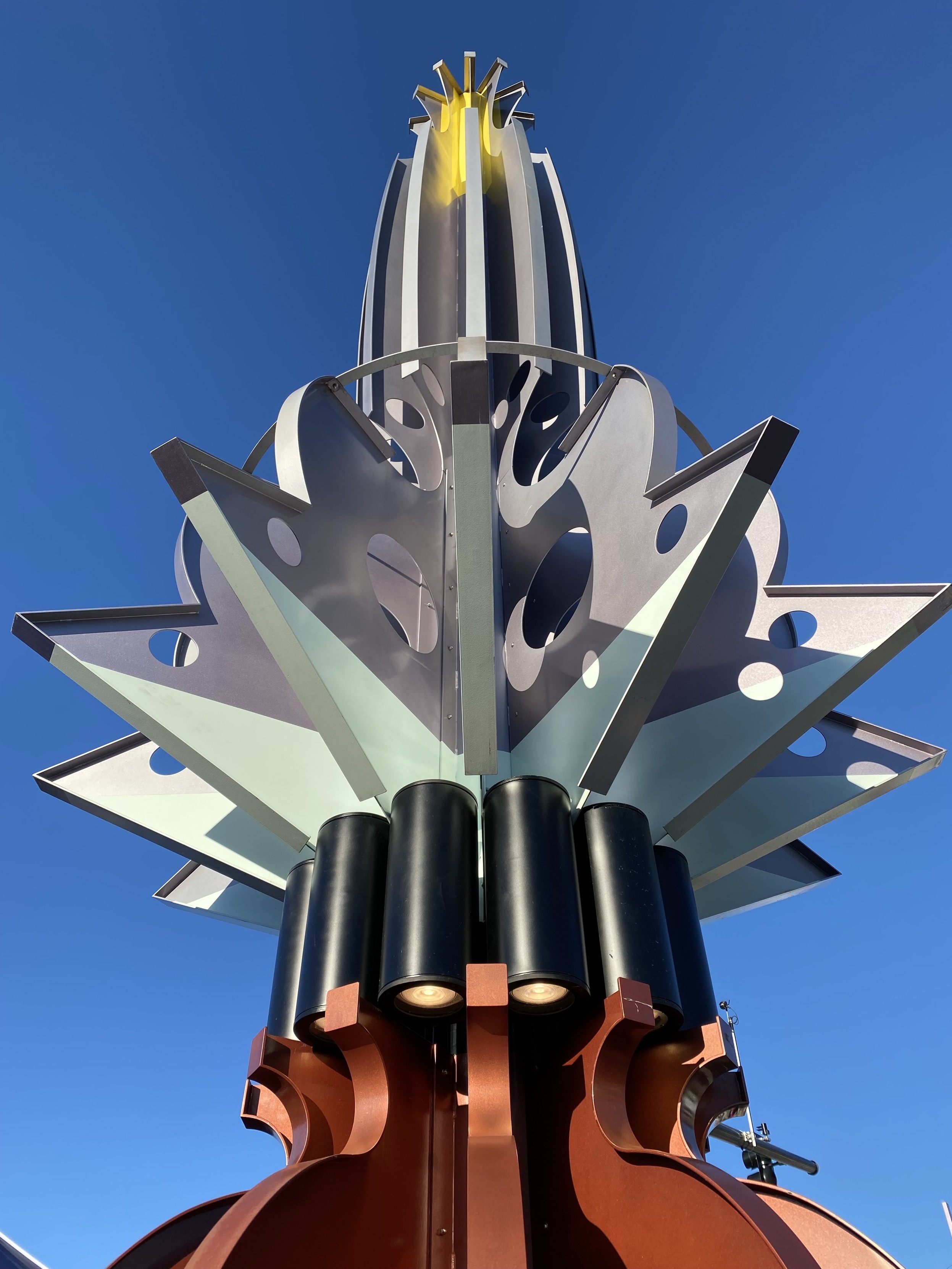 a metal sculpture at the new lynnwood light rail station, in reddish copper, black, and silver-grey, with a yellow burst at the top. it’s vaguely floral and rocket ship in aesthetics. 