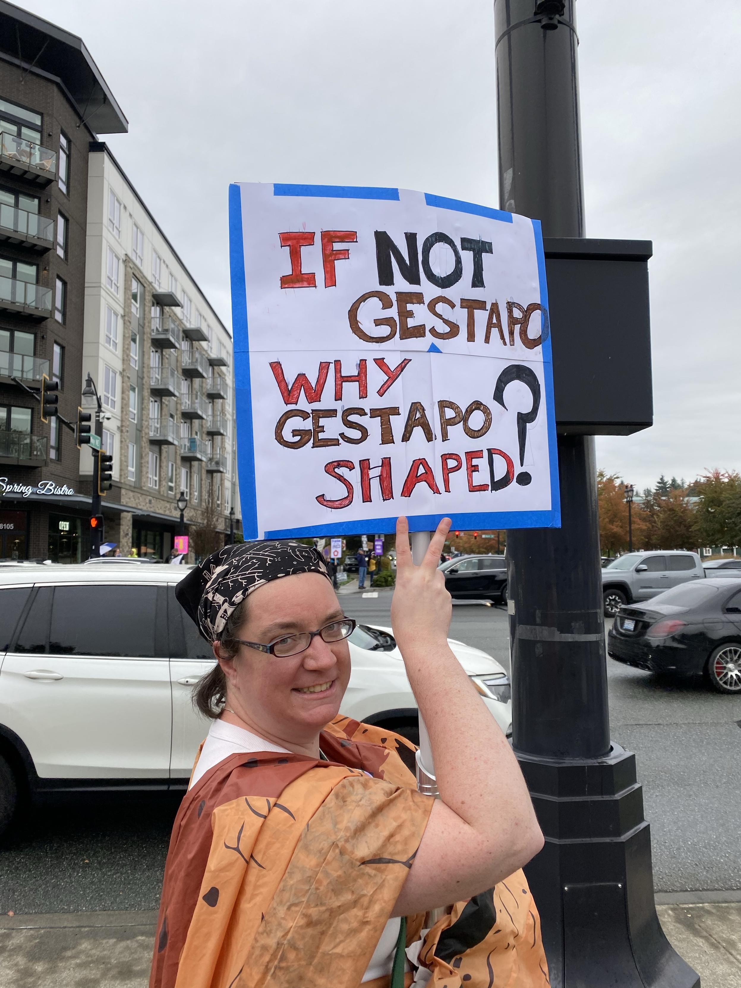 a woman holding up a sign reading IF NOT GESTAPO WHY GESTAPO SHAPED?