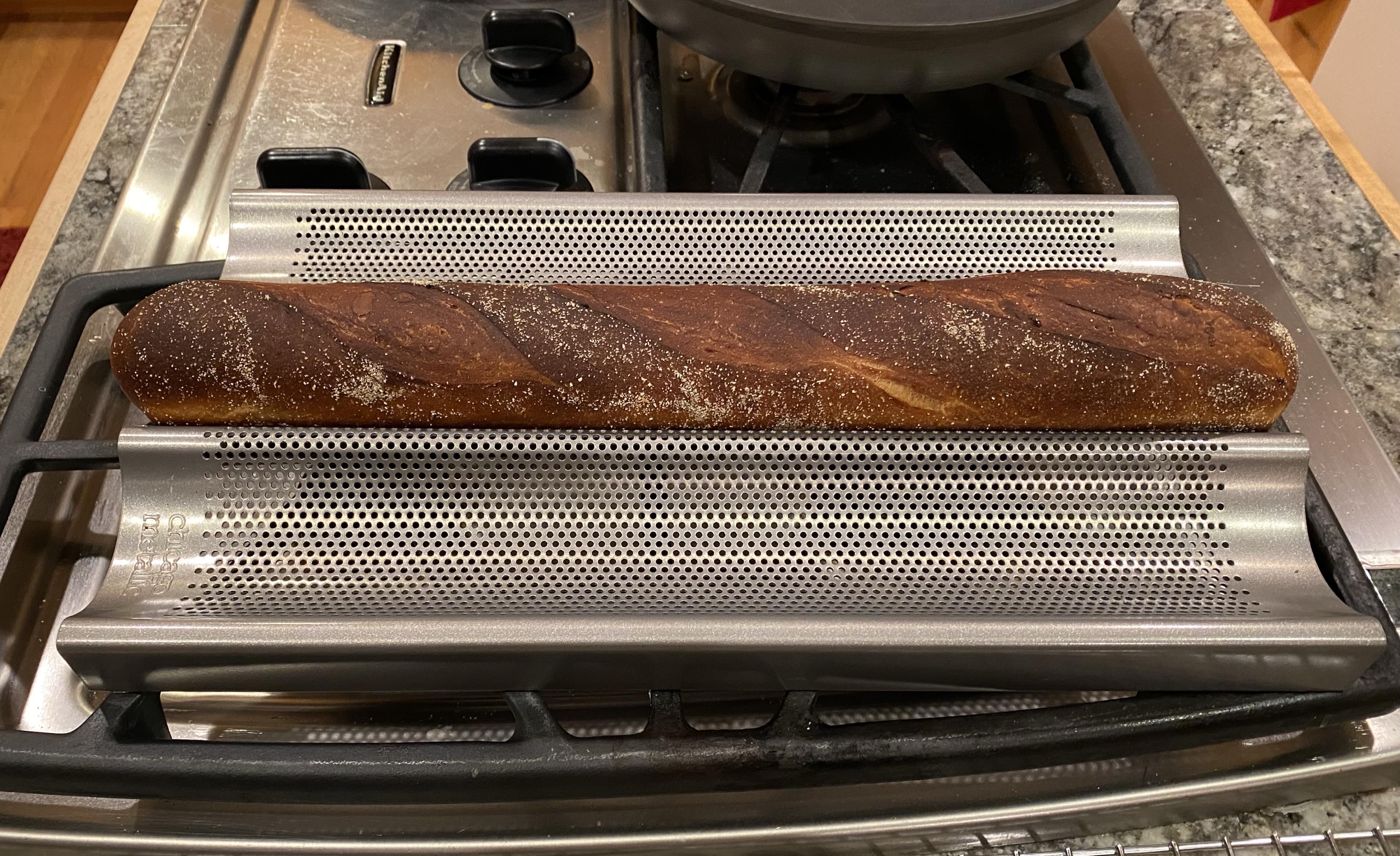 A _very_ brown baguette cooling atop a range with cooling rack in front