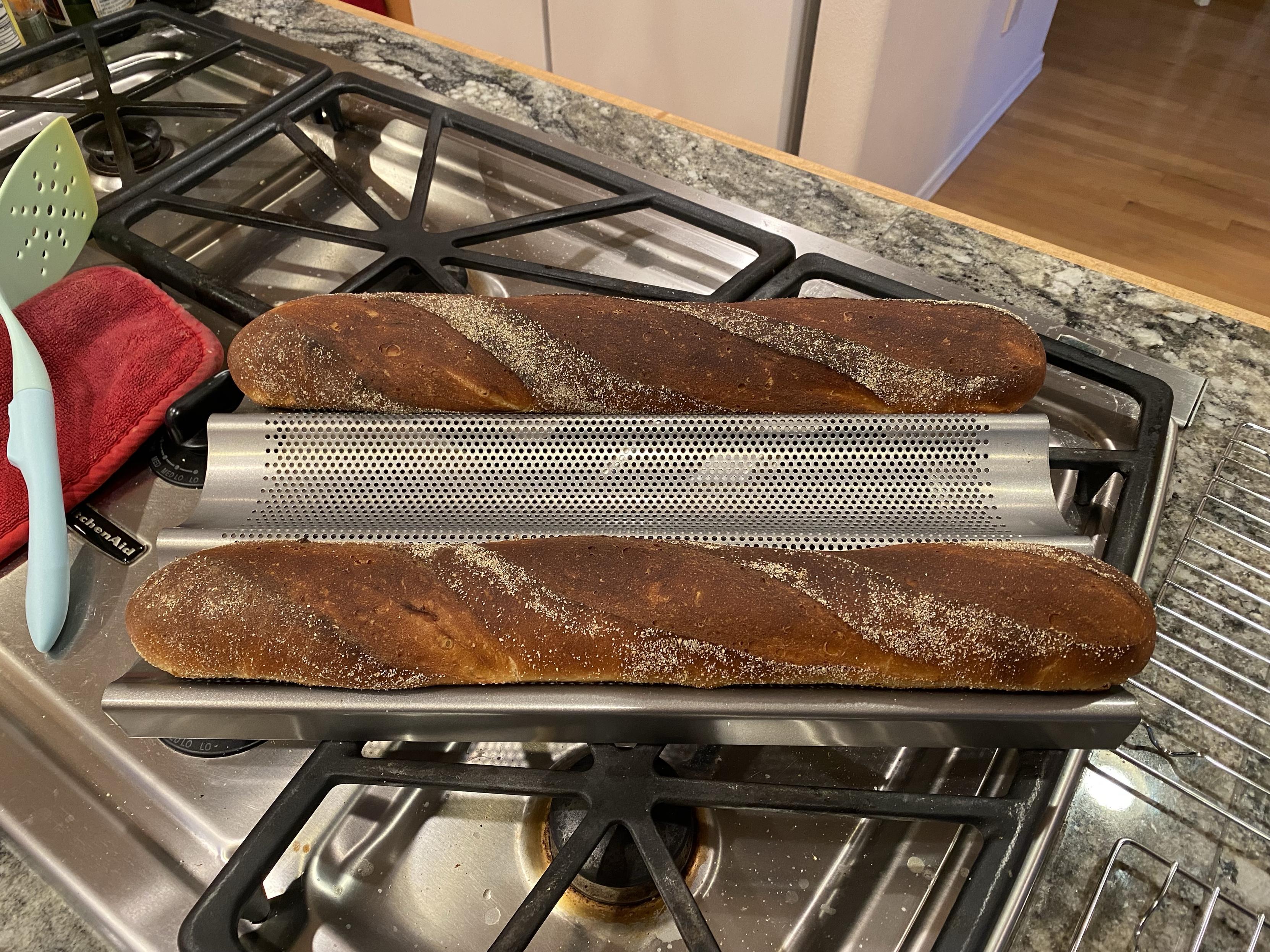 two dark brown baguettes removed from the oven still in baking tray on stovetop, the corn-dusted areas a sprinking of white rotating around the loaves