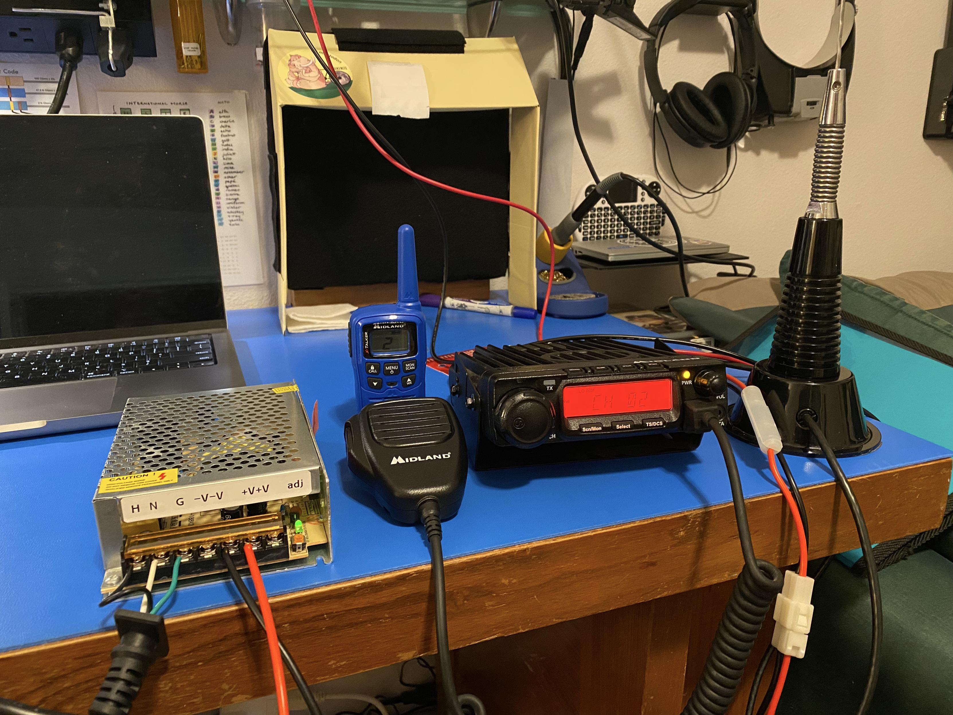 wire cage switching power supply hooked to mains power, GMRS 40W radio hooked to the wire cage switching power supply, full-wave antenna connected to GMRS 40W radio, and blue HT FRS radio, both transceivers on channel 2 with no privacy codes, all on a desktop.