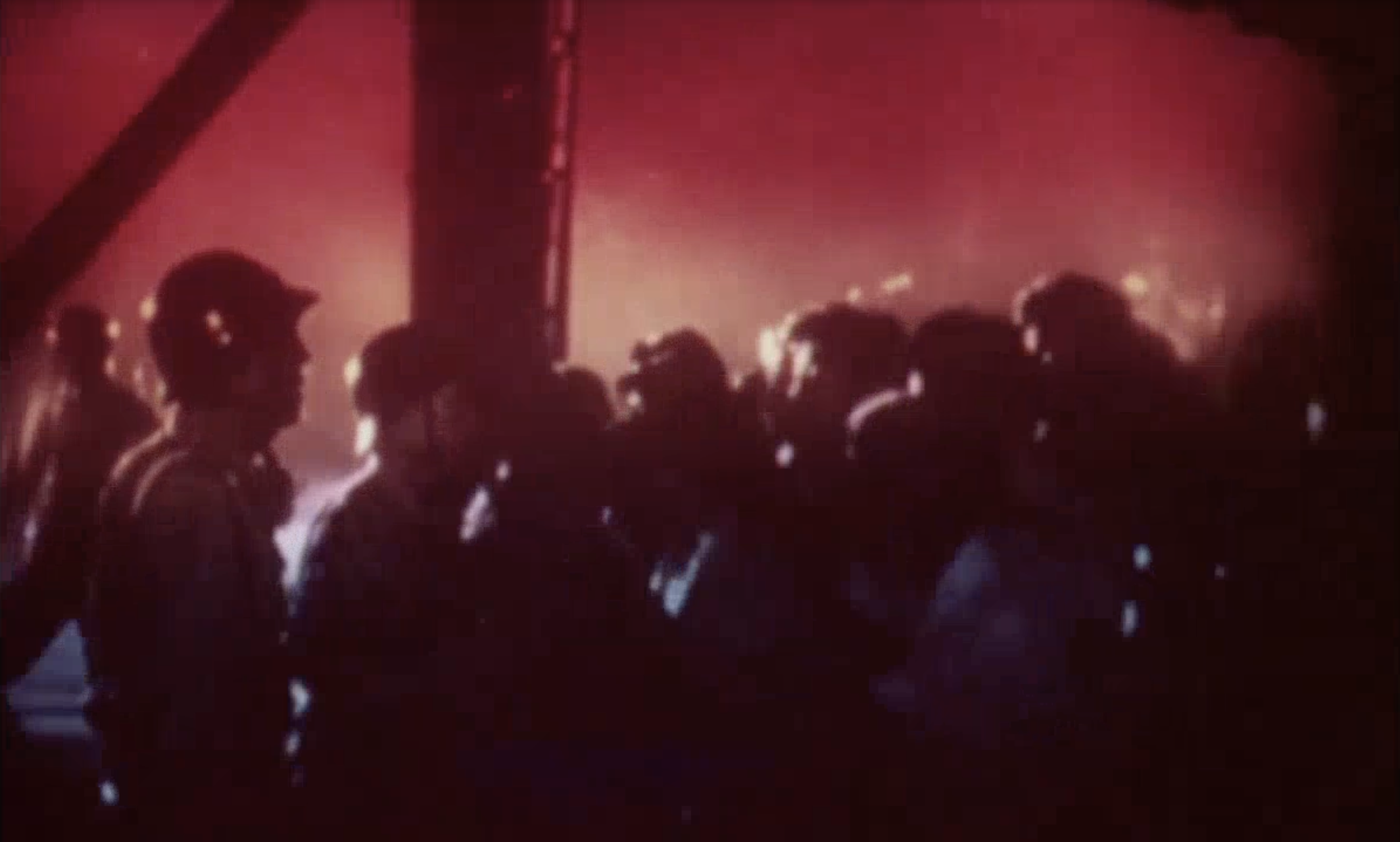 A gel-effect red, orange, and blue hazed crowd evacuation scene from Tokyo as Gojira approaches out of the sea