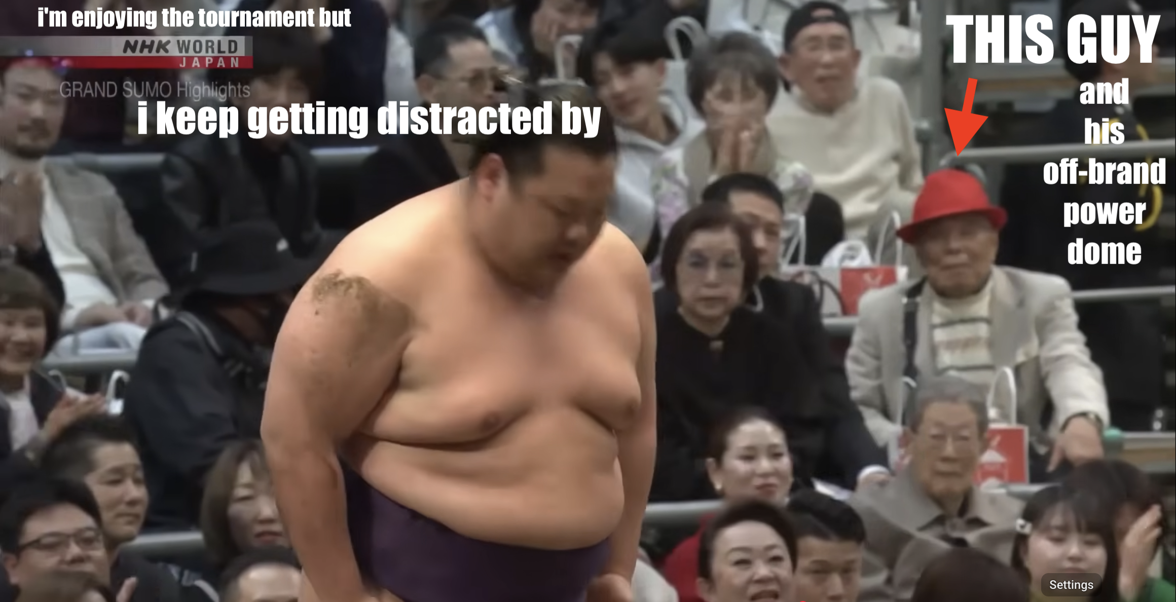 A shot from the aftermath of a sumo bout captioned "i'm enjoying the tournament but / i keep getting distracted by" on the upper left followed by all-caps-with-red-arrow-captioned "THIS GUY AND HIS OFF-BRAND POWER DOME" which is actually just a bright red and rather triangular hat.
