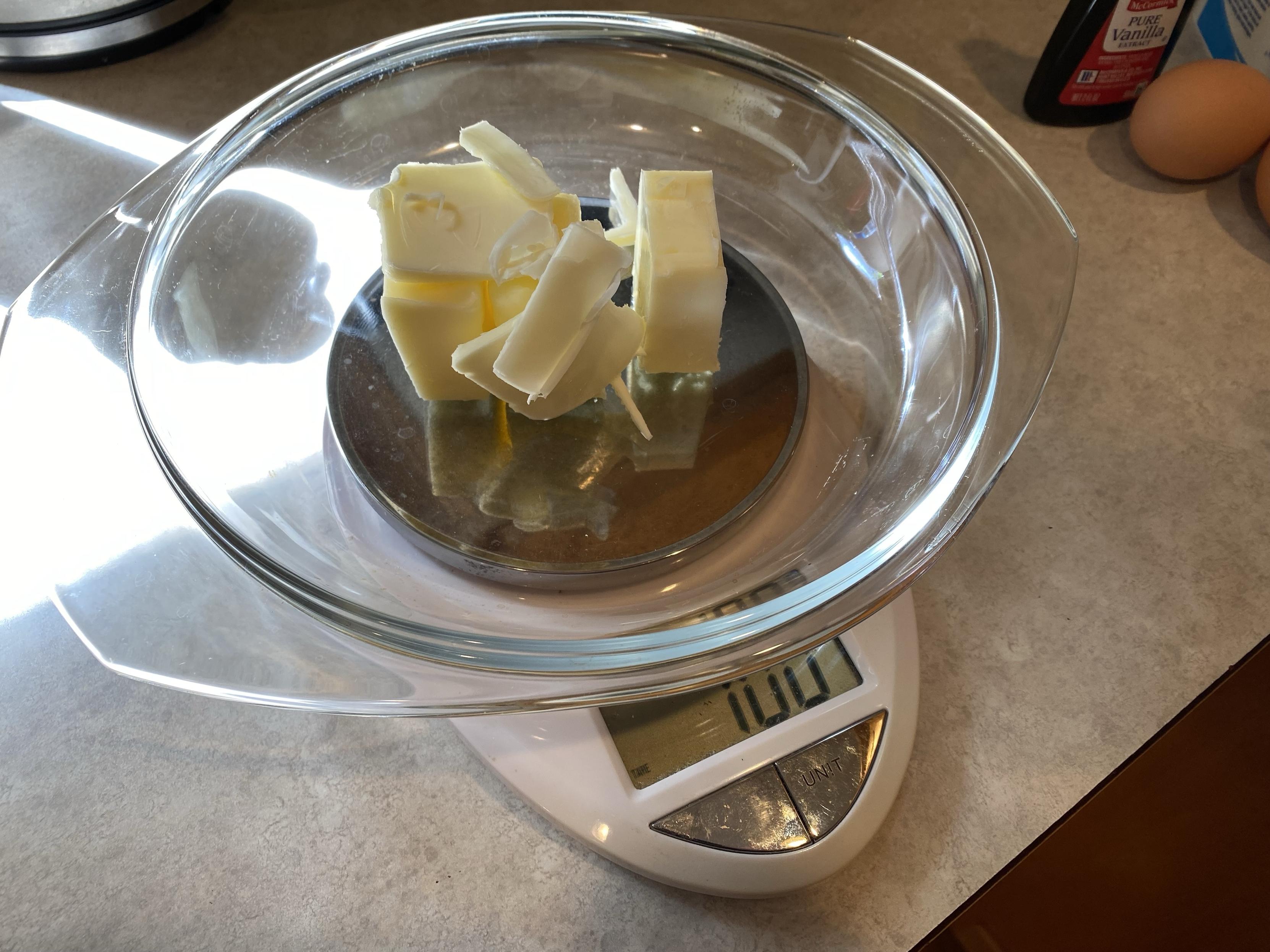 100g butter in a pie plate on a scale showing 100g