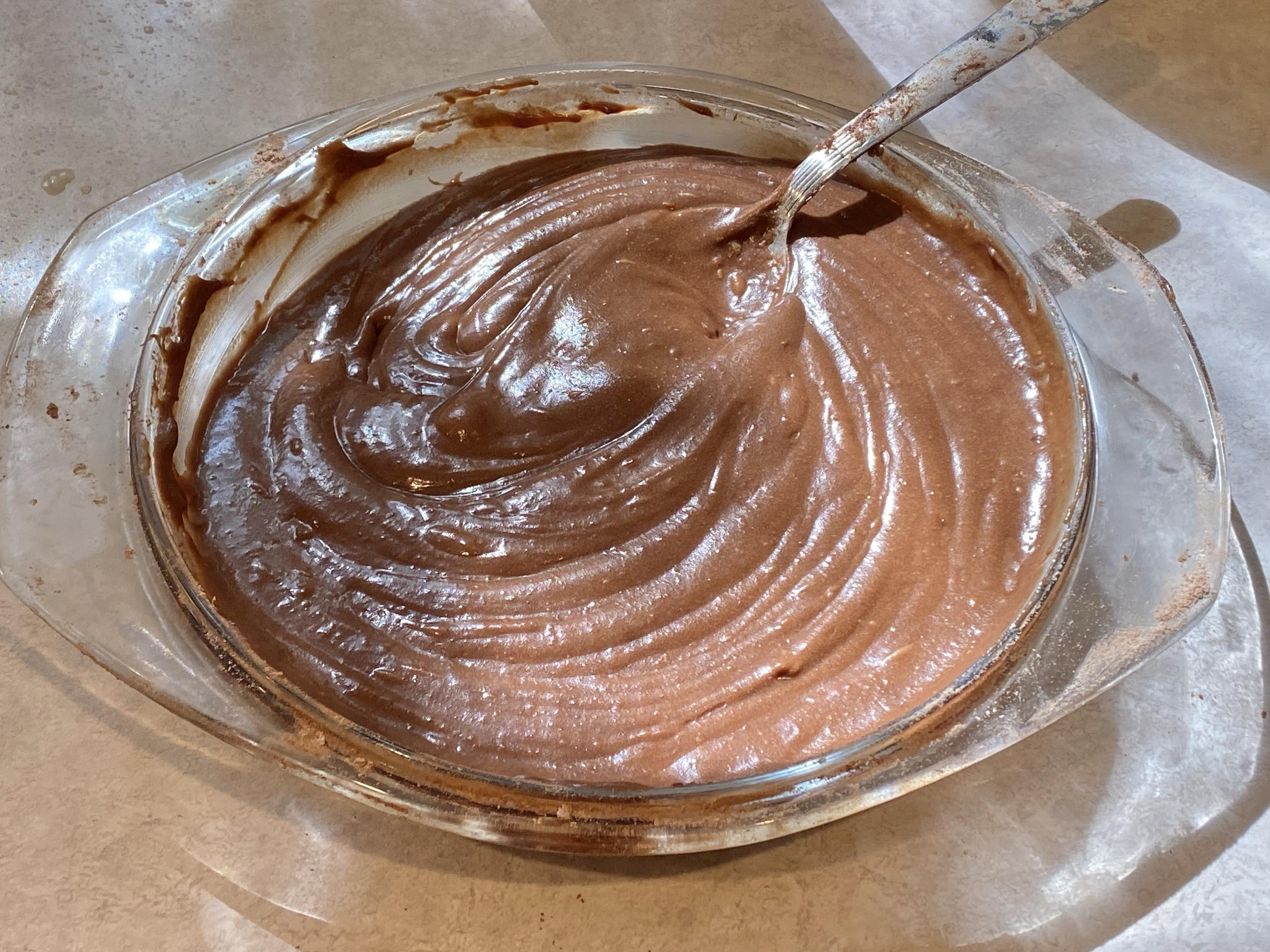 a glass pie plate filled with what looks very much like chocolate pudding with a spoon in it, still being mixed