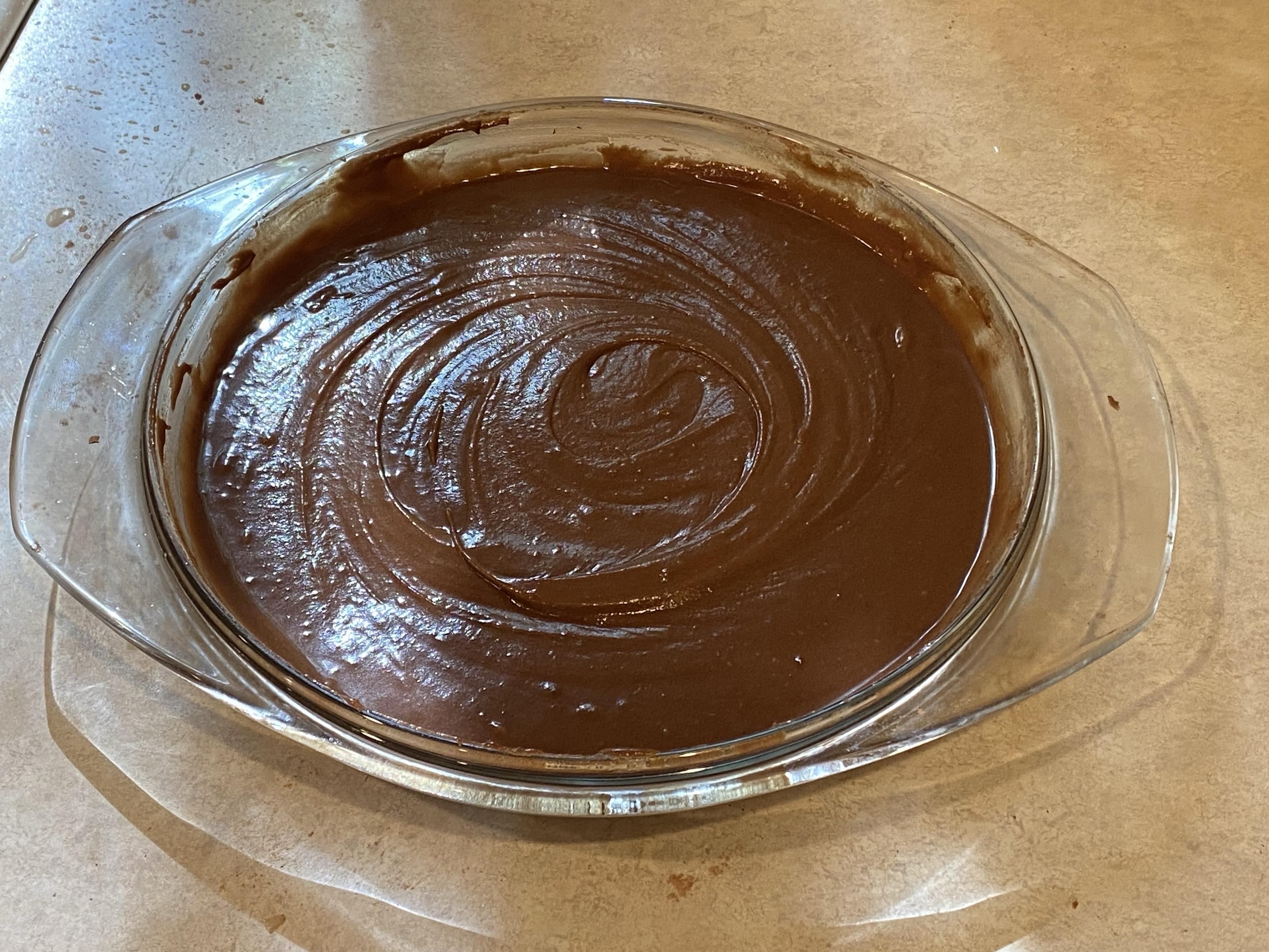 the pie plate full of choco dough with big circular swirls across the surface to level