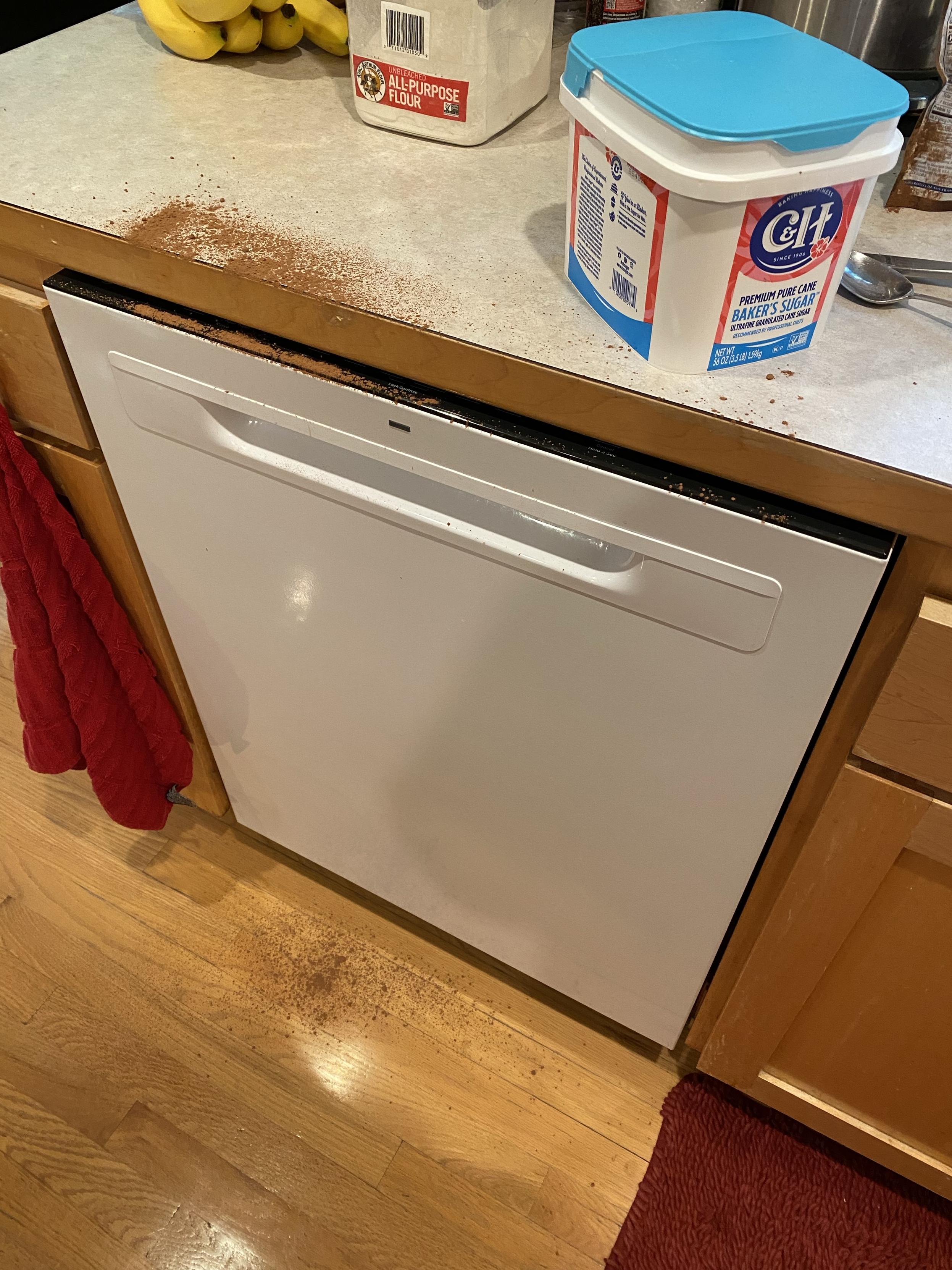 a counter, dishwasher, and floor messed up by cocoa powder exploding everywhere
