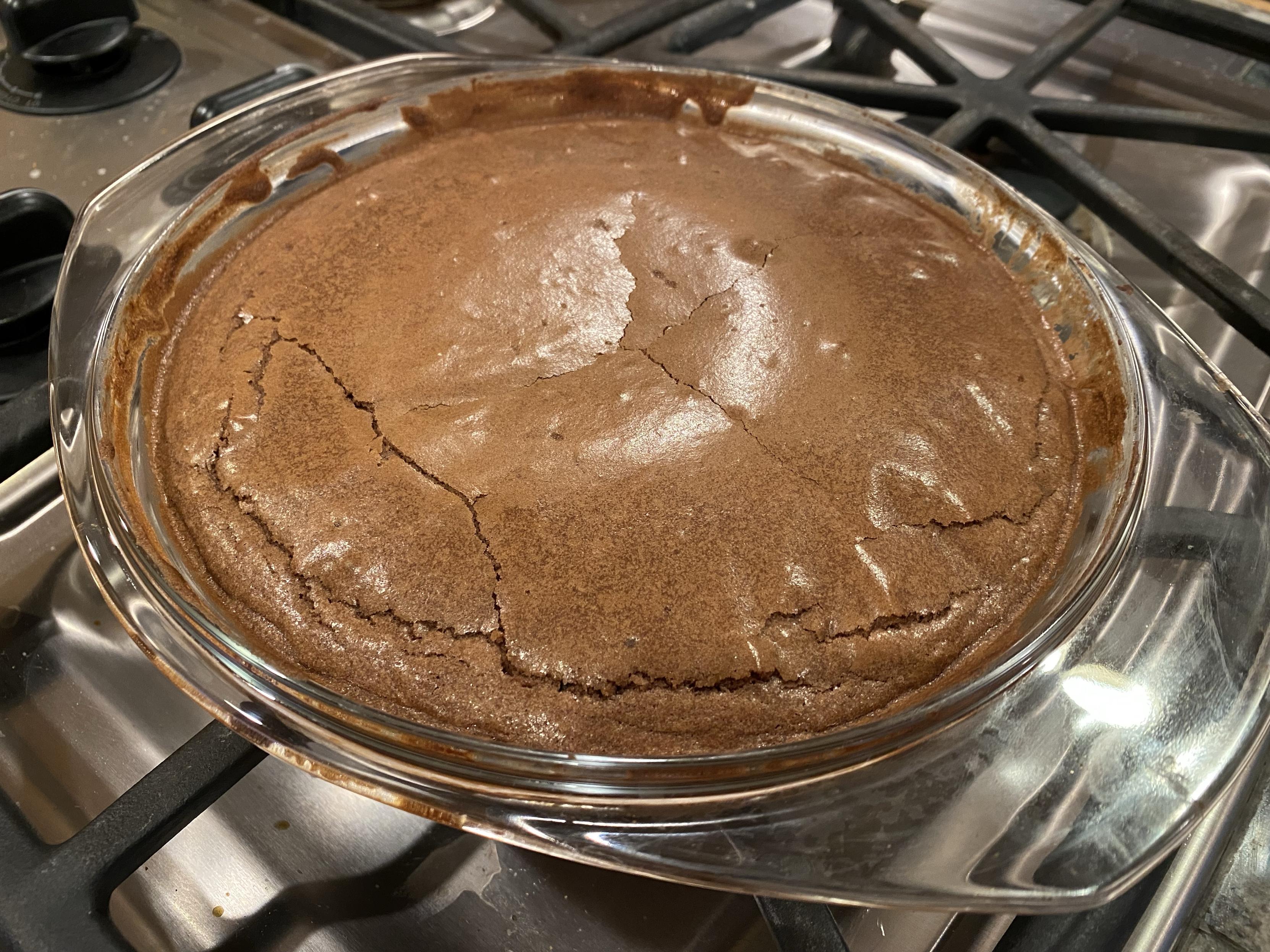 the kladdkaka sitting on the stovetop grates cooling, the centre lowering in as it cools