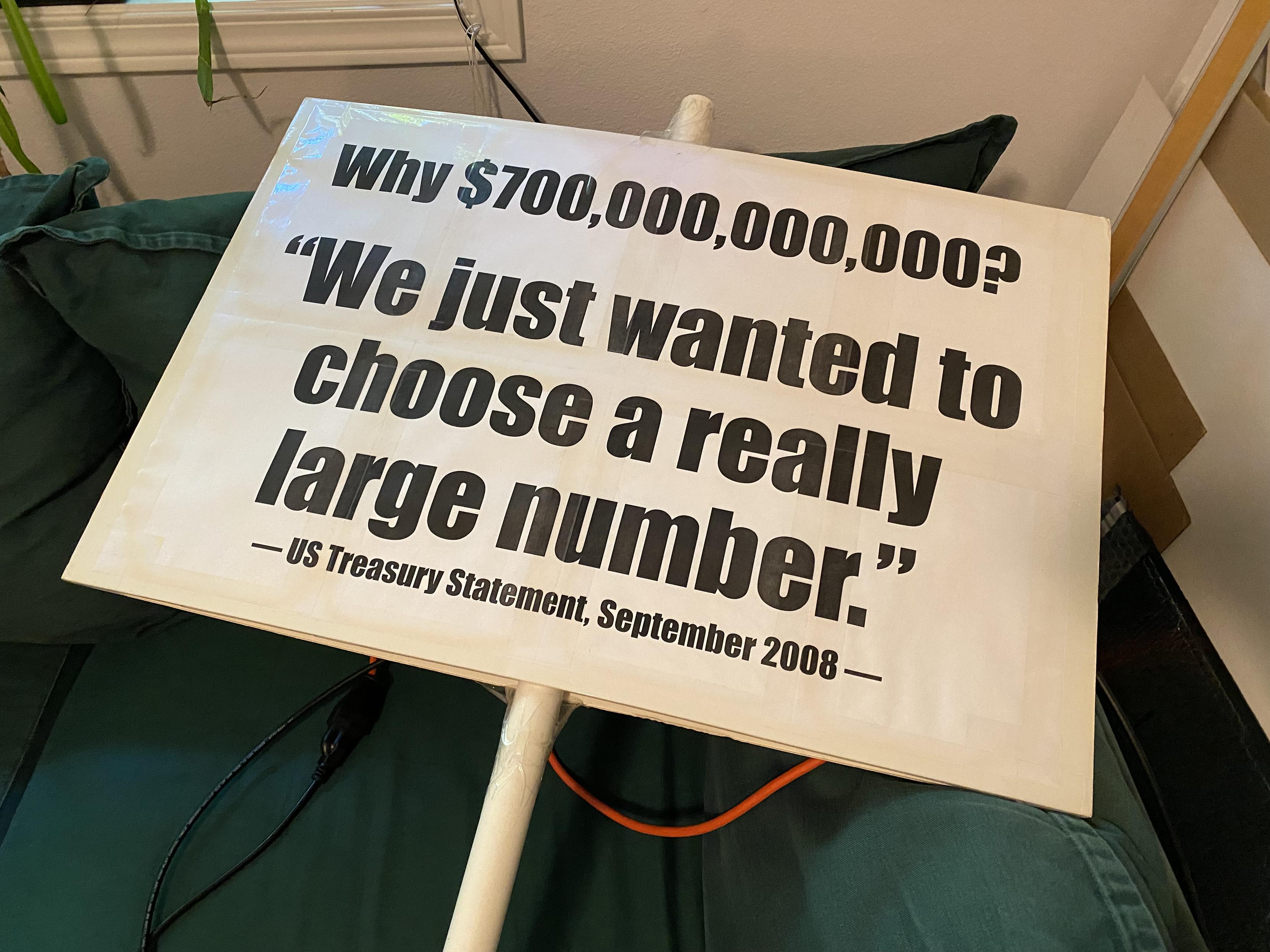 A big and visibly yellowed at the edges protest sign reading "WHY $700,000,000,000? 'We just wanted to choose a really large number.' -- US Treasury Statement, September 2008."