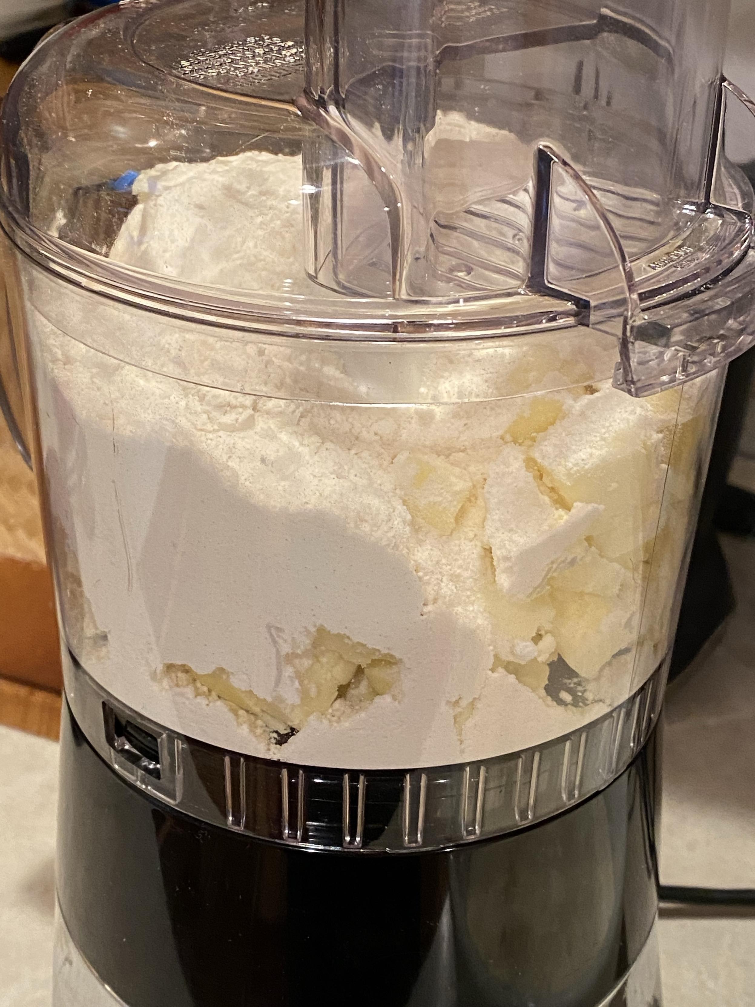 a food processor with the butter cubes and flour ready to be processed