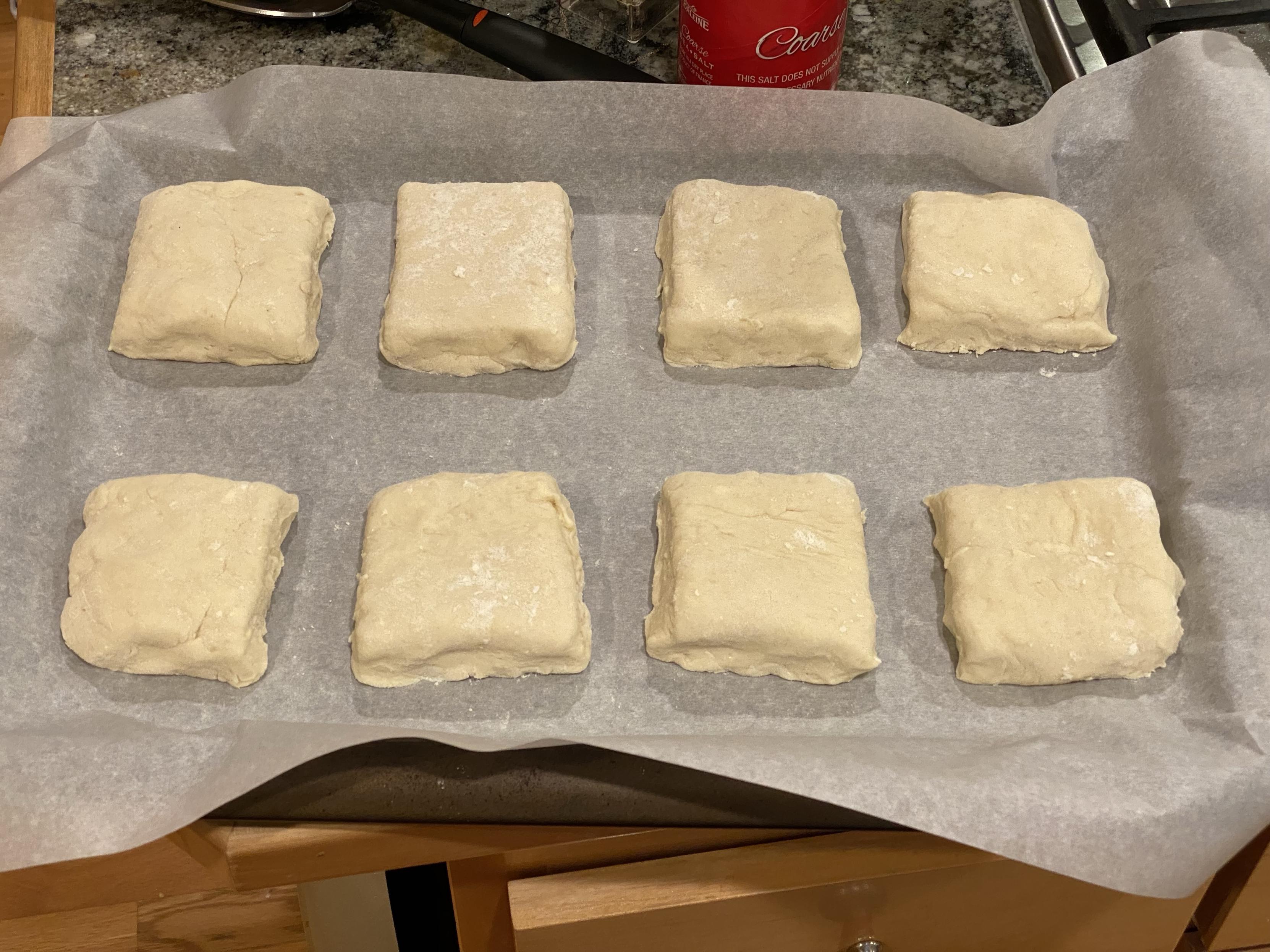 eight biscuit dough squares on parchment paper on a baking tray waiting for the oven to be done preheating