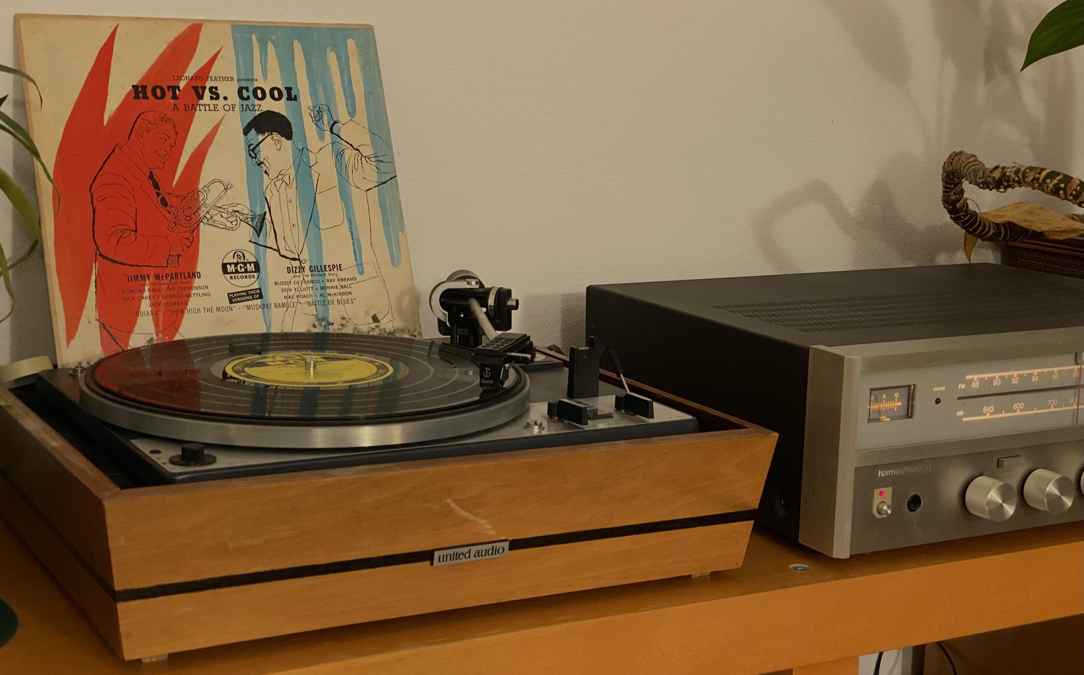 The same receiver, next to which is a United Audio / Dual 1228 semi-automatic turntable with a copy of the 1952 10-inch monophonic microgroove recording "Hot vs. Cool: A Battle of Jazz" between Jimmy McPartland and Dizzy Gillespie, released by MGM Records. The rather damaged cover can be seen leaning behind the turntable platter against the off-white wall.